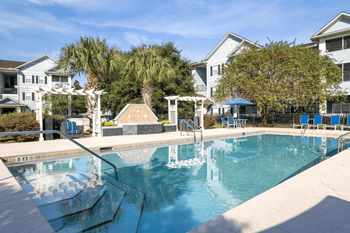 A swimming pool with blue chaise lounge chairs and palm trees in the background